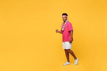 Fototapeta na wymiar Side view full body smiling happy young man 20s he wear pink t-shirt hawaiian lei near hotel pool walk go strolling look camera isolated on plain yellow background. Summer vacation sea rest concept.