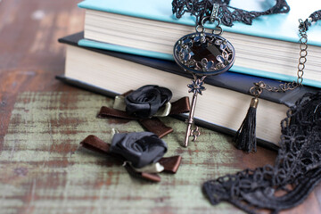 Black and silver decorated key and a stack of books on a wooden table. background. necklace - Powered by Adobe