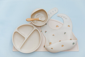 Flat lay composition with silicone baby bib and beige dishware on blue background. Flat lay, top view