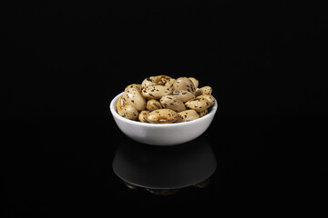 Bean grains in a white plate on a dark table with reflection. Close-up
