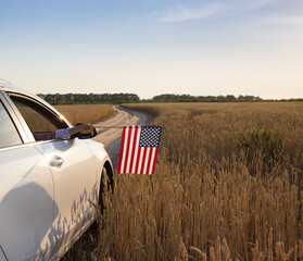 American flag hanging out of a car window in front of a ripe wheat field. USA Independence Day,...