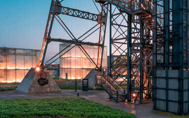 Katowice, Silesia, Poland - August 02, 2021: steel structure of the mining shaft surrounded by modern glass and steel buildings and greenery, evening city landscape