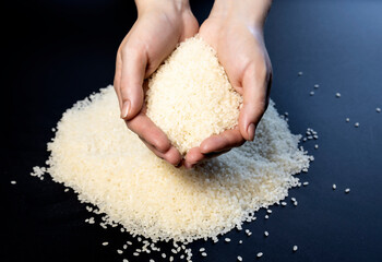 Grains of white rice in female hands on a black background.