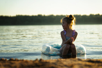 Little girl on the beach sits in the water on an inflatable ring