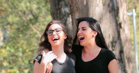 Two girlfriends together walking at the park embracing each other laughing
