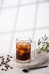 Iced coffee in a cup with ice cubes and grains on a light marble background with morning shadows. The concept of a cold summer drink.  Copy space