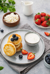 Cottage cheese pancakes with mint, blueberries, strawberries and milk on a gray  background. Healthy and delicious breakfast