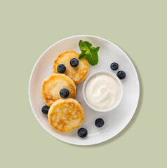 Cottage cheese pancakes with sour cream, mint and blueberries in white plate  on a green background. Healthy and delicious breakfast. Top  .view
