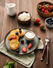 Cottage cheese pancakes with sour cream, milk, blueberries and strawberries on a dark wooden background. Healthy and delicious breakfast. Rustic style