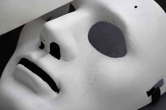 White lying carnival facial mask, closeup, horizontal photo on dark background. Theatre plastic mask, props to hide face, neutral emotions. Design element