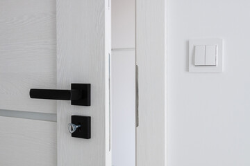 A white wooden door with a black metal handle. Door handle and interior fittings close-up. - obrazy, fototapety, plakaty