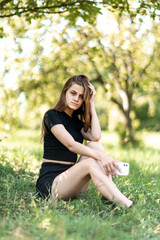 a young and beautiful girl sits in the park in the shade of trees in sunny weather