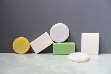 various colored and shapes body bar soaps on green bathroom tile against gray wall, every day...