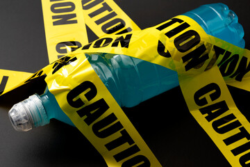Sugary sports drink plastic bottle wrapped in yellow caution tape concept for dangerous liquid...