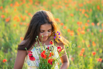 Naklejka premium Beautiful girl in the poppy field. Holding beautiful flowers. summer time. Young girl smells flowers in the field