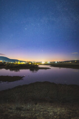 Nightscape of starry spring night over the lake and a luminous town