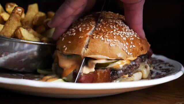 A juicy burger is being cut with a knife 