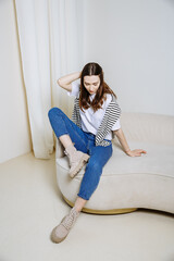 a girl is sitting on a sofa in jeans and a striped sweater in a bright room