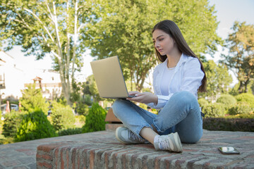 Young woman working on a computer outdoors. Work remotely freelance. Leisure in the park