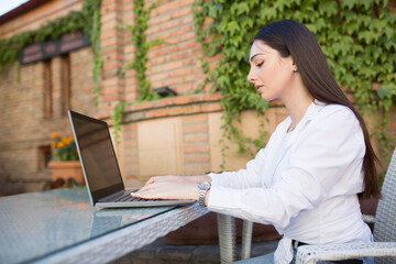 A young woman is sitting in a cafe. Work at the computer outdoors. Freelance