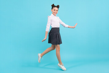 Excited jumping teenager. Happy schoolgirl, positive and smiling emotions of teen girl. Full length jump of teenager girl on blue isolated studio wear casual skirt and shirt.