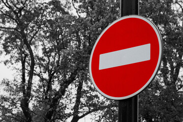 Colorful road traffic sign Entry is prohibited on back and white background of sky aqnd trees foliage. Sign is also known as ''The Brick''. It restricts vehicles movement in this direction.