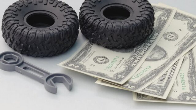 car repair and maintenance,tires replacement. rubber black tires from toy car grey little plastic wrench on dollar bills background.one back tire is rolling on dollars.save money,service costs concept