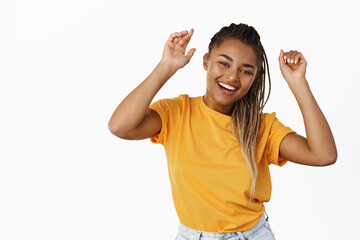 Happy, beautiful african american girl dancing carefree, smiling and laughing with joy, standing in yellow tshirt over white background