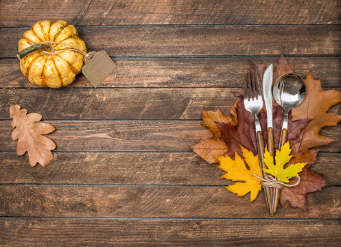 Thanksgiving Day background with copy space. Fall table place setting with silverware decorated with autumnal leaves and decorative pumpkin on rustic wooden background.