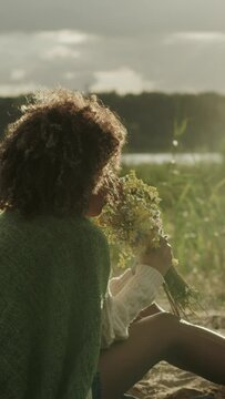 A young woman sitting on the blanket smelling flowers