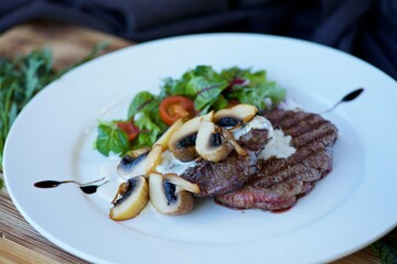 Pieces of fried meat lie on a white plate and drizzled with white sauce. Decorated with vegetables, mushrooms and herbs. The concept of recipes from the restaurantf.