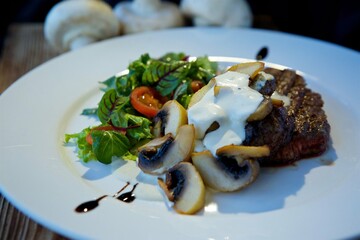 Pieces of fried meat lie on a white plate and drizzled with white sauce. Decorated with vegetables, mushrooms and herbs. The concept of recipes from the restaurantf.