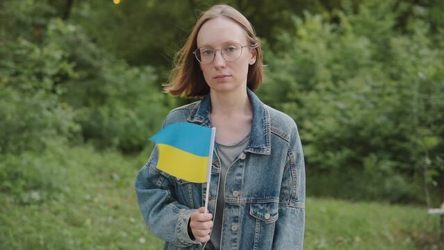 Portrait of a woman 20s 30s activist with the flag of Ukraine outdoors looks at the camera. 