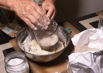 an elderly woman sifts flour to make dough for homemade pies