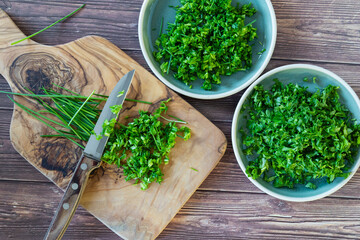 Fresh and chopped spicy parsley and chives herbs on cutting board, top view. - obrazy, fototapety, plakaty