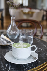 A cup of matcha latte is on the table in a cafe. Delicious green matcha tea in a green cup close-up. Japanese hot milky beverage. Healthy Matcha Tea Made with Organic Ingredients