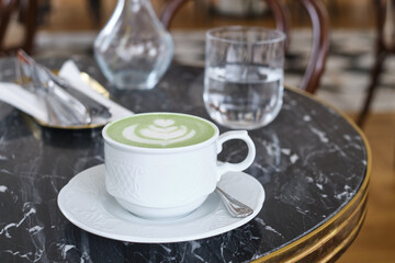 A cup of matcha latte is on the table in a cafe. Delicious green matcha tea in a green cup...