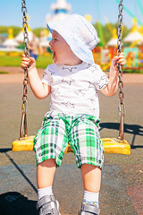 joyful kid rides swing on outdoor playground on sunny day, happy little kid in play park in the summer