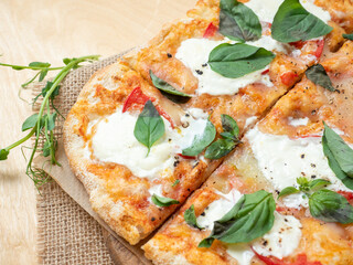 Close-up of a fresh hot Roman pizza with tomatoes and strachatella cheese on a raw wooden...