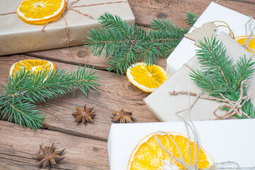 Fototapeta na wymiar Christmas presents or gift box wrapped in kraft paper with decorations, pine cones, dry orange orange slices and fir branches on a rustic wooden background. Holiday concept