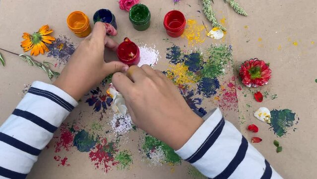 Close-up of children's hands that create a drawing using a flower by poking. What to do with children in kindergarten or school camp in the summer.
