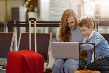 Mom and son in the airport lounge watching something on a laptop before the flight