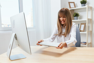 Irritated blonde businesswoman screaming to keyboard Raging after computer software crash error at...