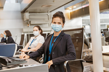 Woman airline employee wearing face mask while working at airline check in counter in airport