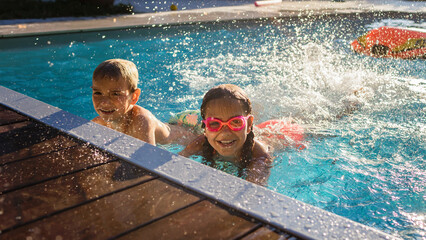 Refreshing at heat weather. Cheerful children in googles smiling while playing in swimming pool at...