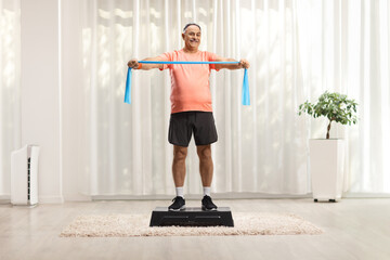 Mature man in sportswear exercising with a stretch strap on a step aerobic platform in a room