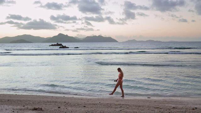 slender woman in a swimsuit walks along a paradise beach with palm trees and turquoise sea