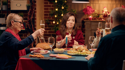Happy close relatives clinking sparkling wine while celebrating winter feast together. Cheerful multicultural family members toasting champagne while enjoying Christmas dinner at home.