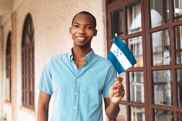 Portrait of a young african man looking at camera holding a small honduras flag.