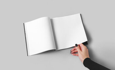 A woman holds a magazine or catalog in a square format with white sheets in her hand. Mockup with...